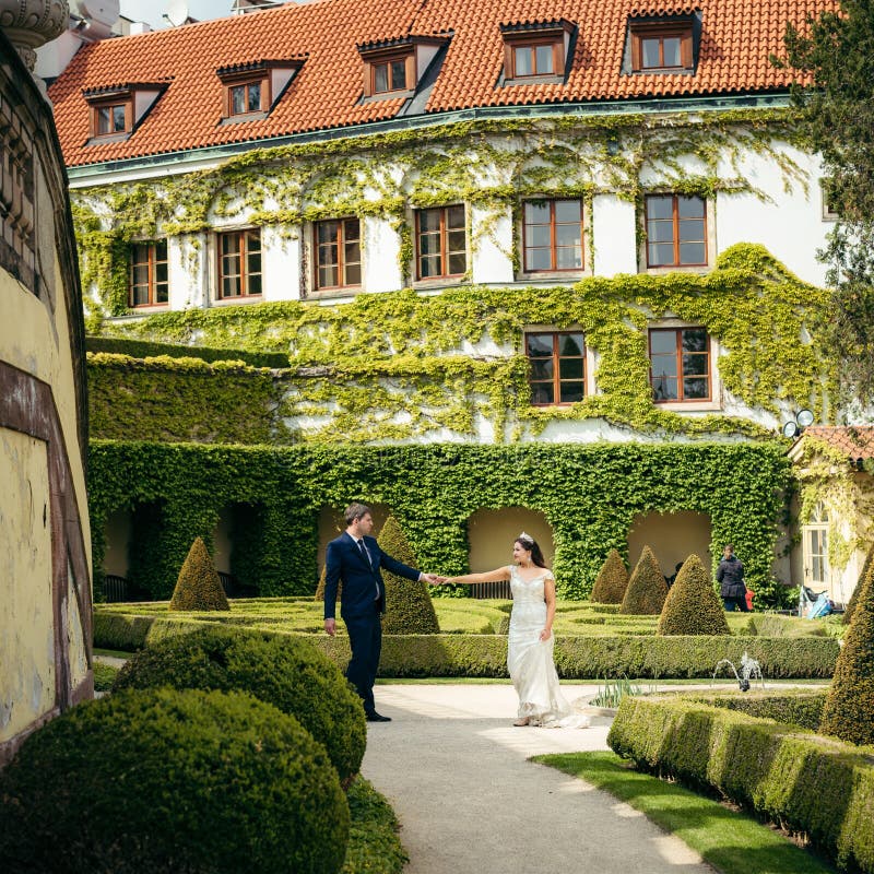 Opinión integral los recienes casados alegres que llevan a cabo las manos mientras que pasa su tiempo en el jardín viejo en Praga foto de archivo libre de regalías Opinión integral los recienes casados alegres que llevan a cabo las manos mientras que pasa su tiempo en el jardín viejo en Praga foto de archivo libre de regalías