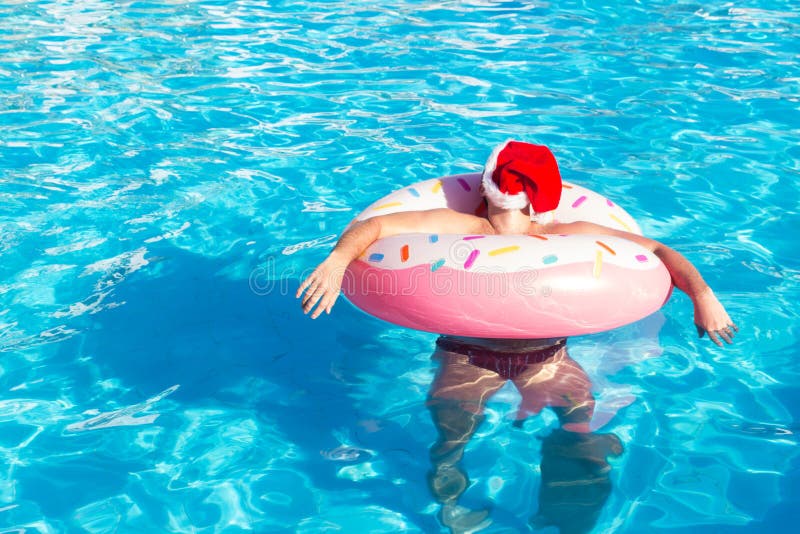 Opinión superior el individuo bebido joven en nadada del sombrero de la Navidad con el círculo rosado en piscina individuo borrac imagen de archivo libre de regalías Opinión superior el individuo bebido joven en nadada del sombrero de la Navidad con el círculo rosado en piscina individuo borrac imagen de archivo libre de regalías