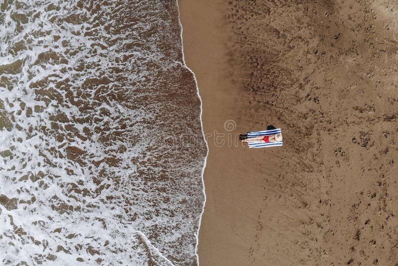 Opinión superior la mujer en el sombrero rojo del bikini y de paja bronceado en la toalla en la playa del océano con la arena neg imagenes de archivo Opinión superior la mujer en el sombrero rojo del bikini y de paja bronceado en la toalla en la playa del océano con la arena neg imagenes de archivo