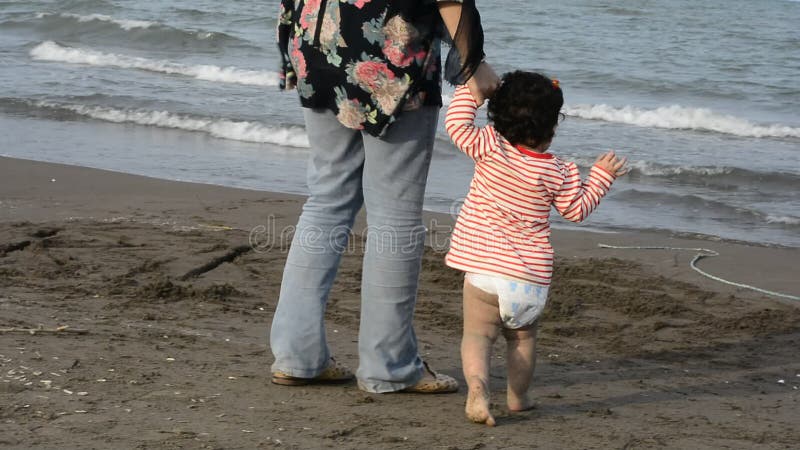 Opinión trasera la madre y el niño joven con el pañal que caminan en el parenting de la playa y el concepto de enseñanza almacen de video