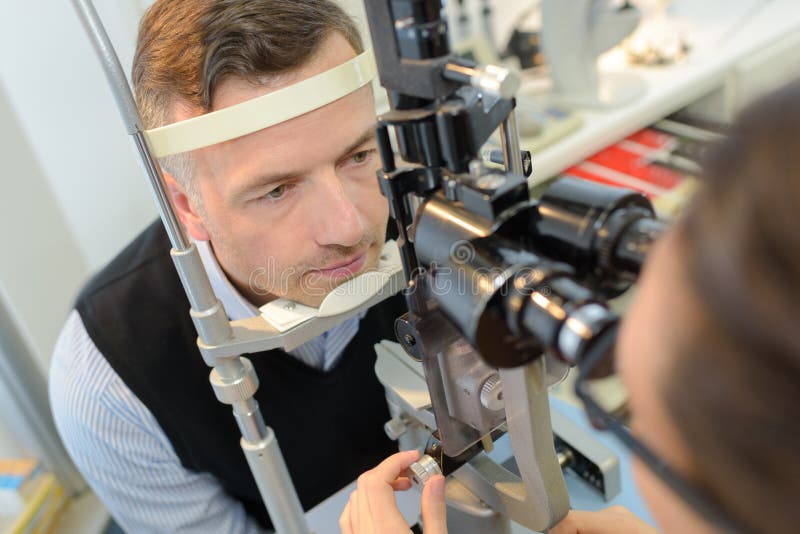 Optiker i kirurgi som ger manögonprovet arkivfoto Optiker i kirurgi som ger manögonprovet arkivfoto