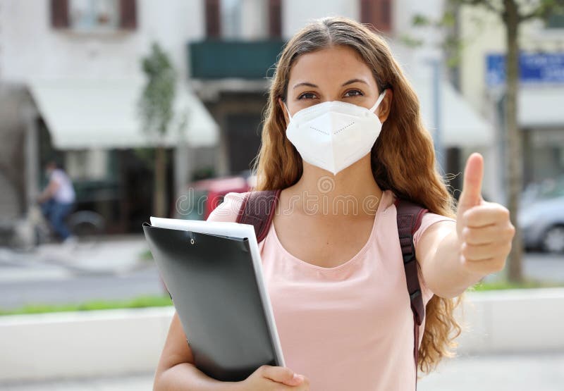 Optimistic student girl back to school with protective mask shows thumb up