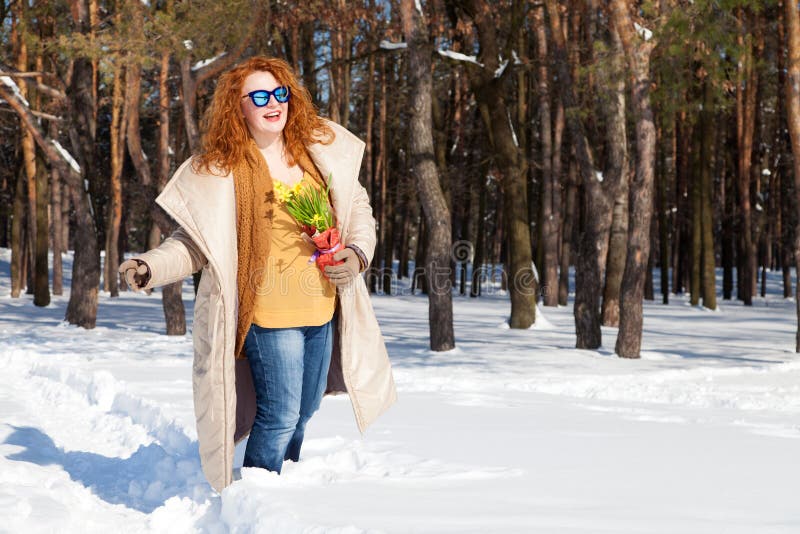 Optimistic woman walking through snowy forest with bouquet of yellow narcissus stock photos Optimistic woman walking through snowy forest with bouquet of yellow narcissus stock photos