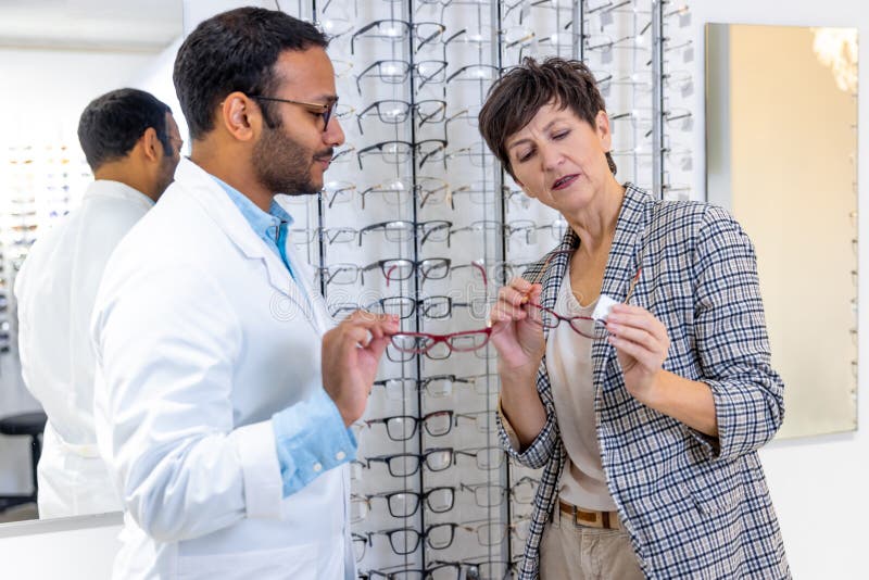 Optometrista maschio che aiuta una donna a scegliere gli occhiali immagini stock