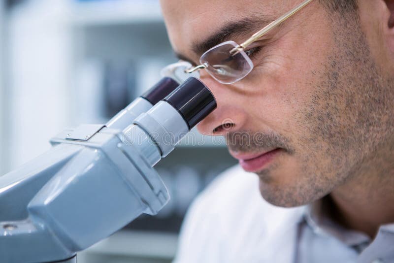 Optometrista maschio che guarda tramite il microscopio immagine stock