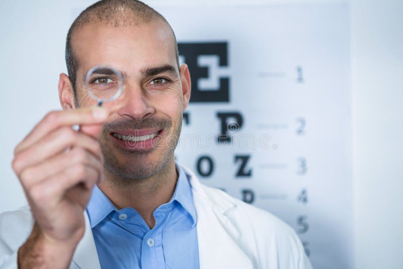 Optometrista maschio che guarda tramite la lente d'ingrandimento fotografia stock