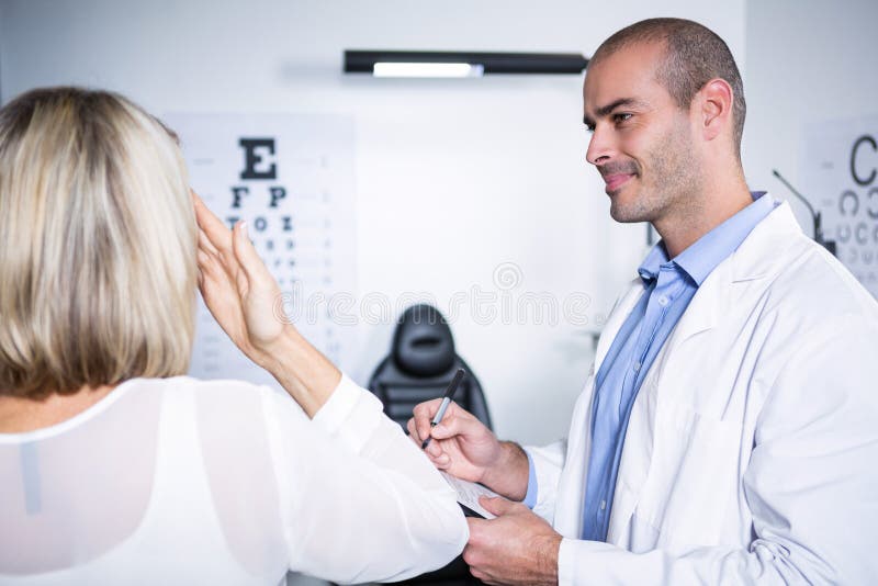 Optometrista maschio che prende la prova dell'occhio del paziente femminile fotografie stock libere da diritti