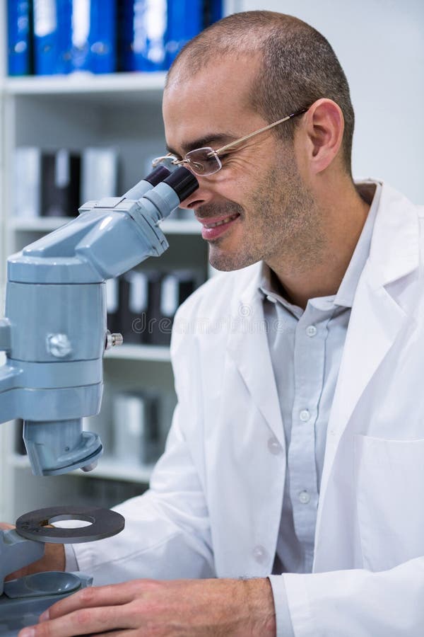 Optometrista maschio sorridente che guarda tramite il microscopio immagini stock