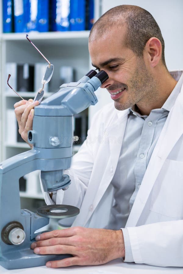 Optometrista maschio sorridente che guarda tramite il microscopio fotografia stock libera da diritti