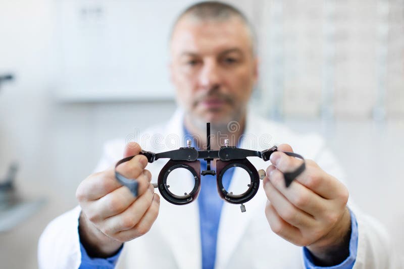 Optometrista professionale, in posizione di lavoro, con un ottometro, con una carta di controllo oculare sullo sfondo. Professiona immagine stock