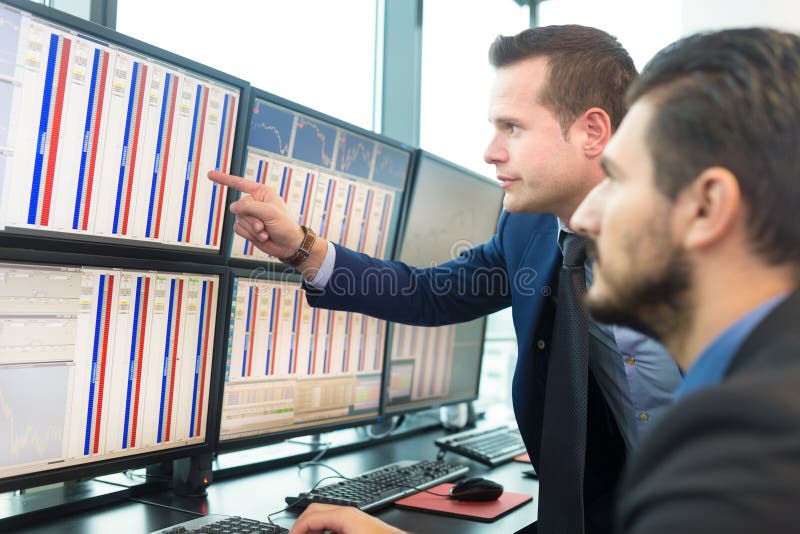 Businessmen trading stocks. Stock traders looking at graphs, indexes and numbers on multiple computer screens. Colleagues in discussion in traders office. Businessmen trading stocks. Stock traders looking at graphs, indexes and numbers on multiple computer screens. Colleagues in discussion in traders office.