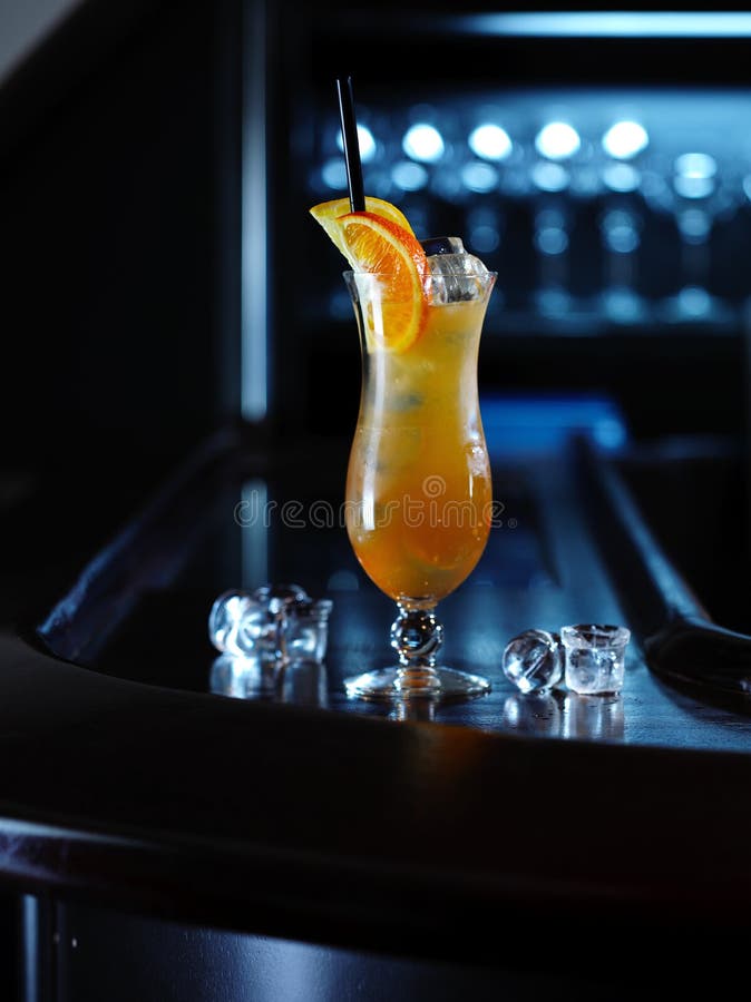 Orange cold alcohol cocktail in transparent glass and ice pieces on the bar table. Orange cold alcohol cocktail in transparent glass and ice pieces on the bar table