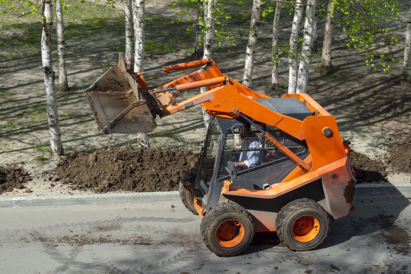 An orange-colored wheel loader delivers ground to an alley with trees royalty free stock images An orange-colored wheel loader delivers ground to an alley with trees royalty free stock images