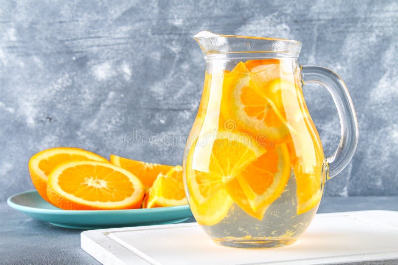 Orange detox water in a pitcher on a gray concrete background. Healthy food, drinks.