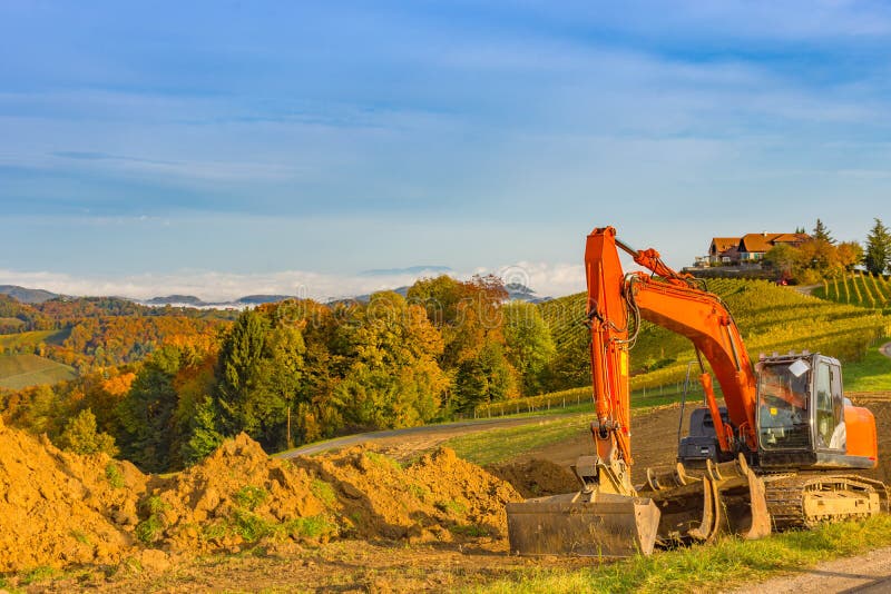 Orange digger/excavator machine excavating the vineyards farmland for maintenance work or to prepare it for new planting in South Styria, Austria, in autumn.