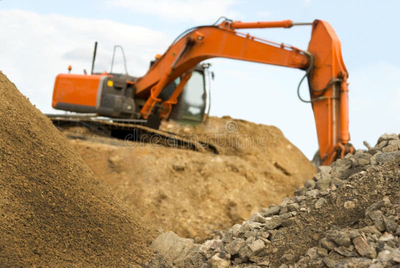 Orange earth digger on a heap of sand. Focus on the sand in the foreground. Orange earth digger on a heap of sand. Focus on the sand in the foreground