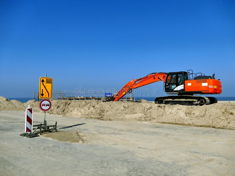 Orange excavator on pile of sand with road signs on construction site with blue sky