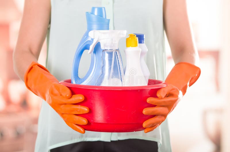 Closeup orange gloves holding red bucket of cleaning products and smiling to camera, housecleaning concept. Closeup orange gloves holding red bucket of cleaning products and smiling to camera, housecleaning concept.