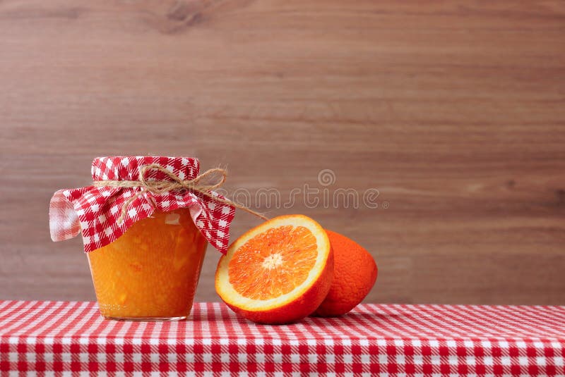 Orange jam in glass jar and orange halves on a red checkered tablecloth. Wooden background stock images Orange jam in glass jar and orange halves on a red checkered tablecloth. Wooden background stock images