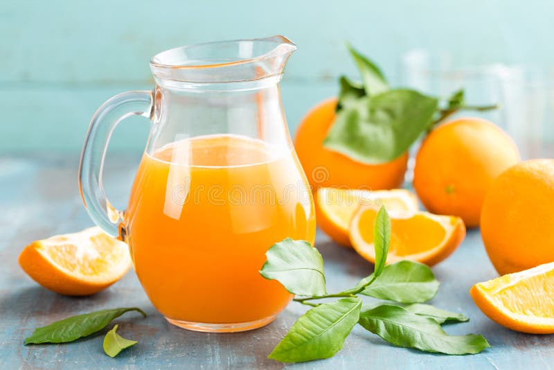 Orange juice in glass and fresh fruits with leaves on wooden background