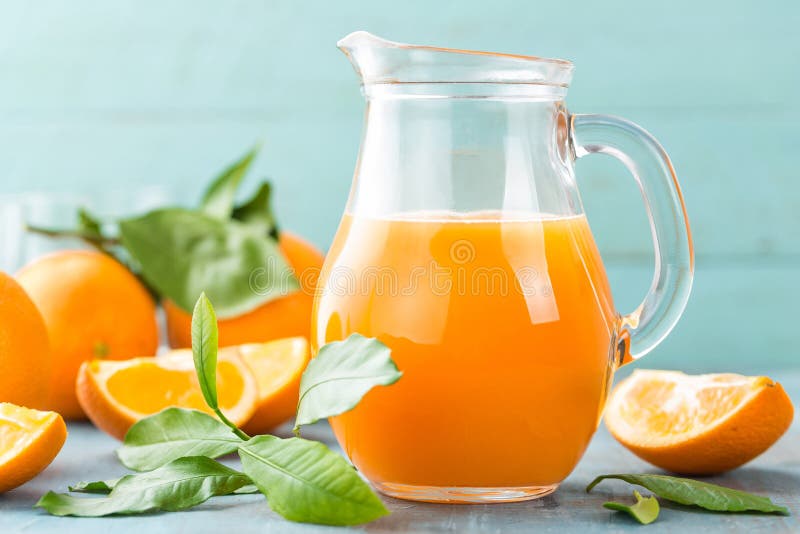 Orange juice in glass and fresh fruits with leaves on wooden background