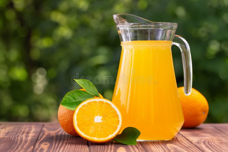 Naranja jugo en vaso jarra sobre el de madera mesa afuera.