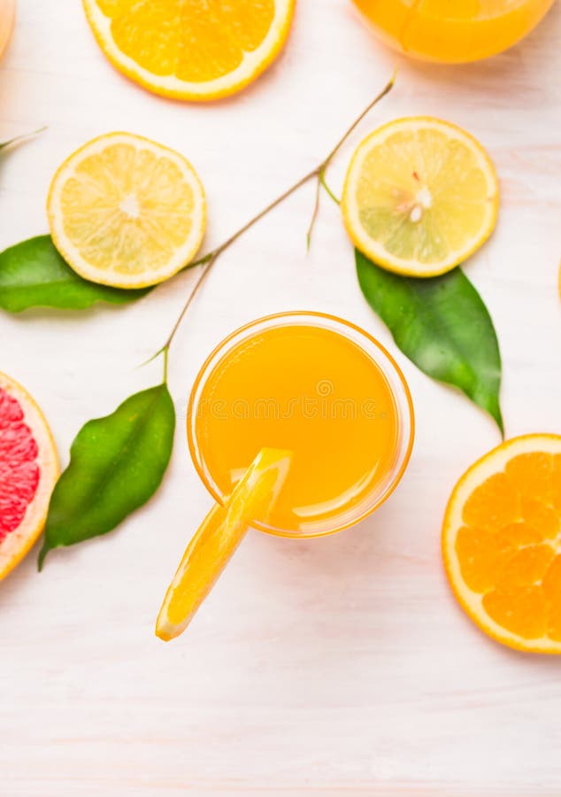 Orange juice glass with slices of citrus and green leaves on white wooden