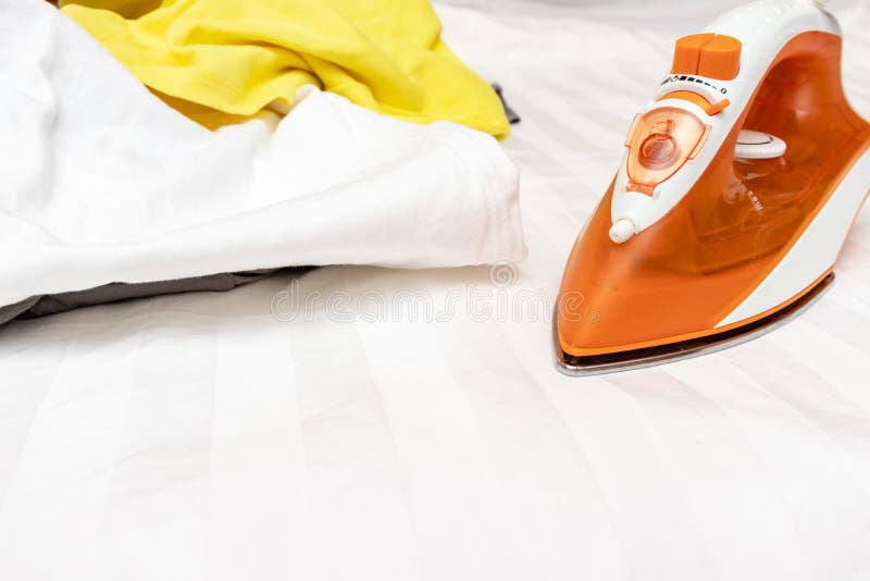 An orange modern electrical iron and a heap of unironed clothes close up with copy space stock image