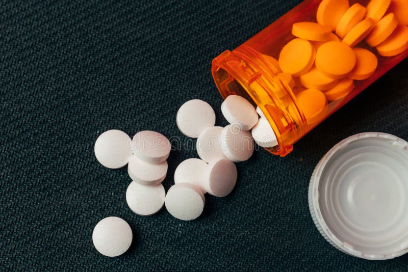 White Pills and Orange Pill Bottle on Gray Table, Macro Shot