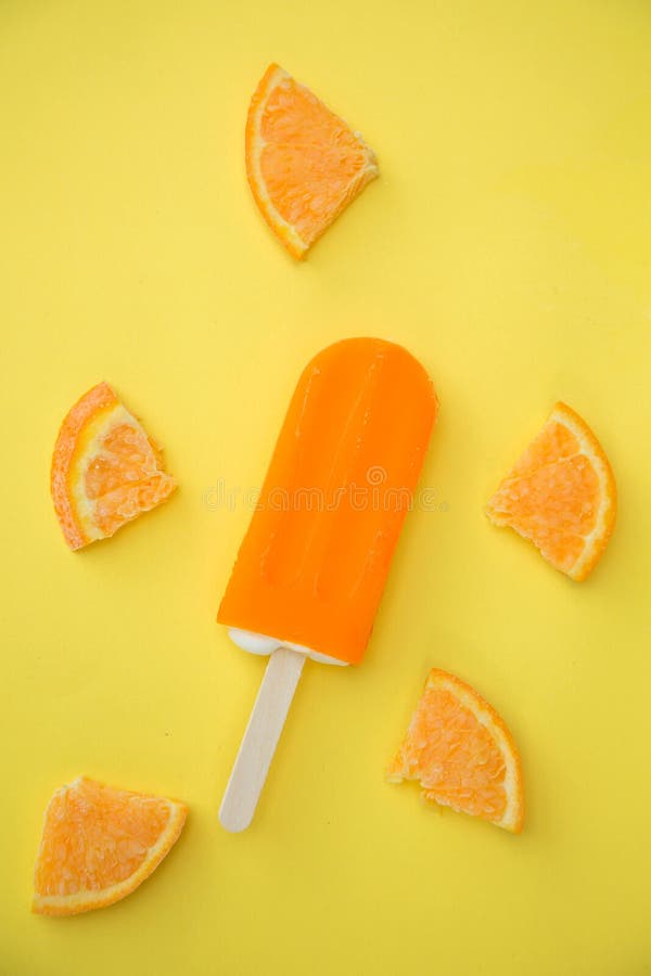 Orange popsicle with few slice of orange on a yellow background. Orange popsicle with few slice of orange on a yellow background