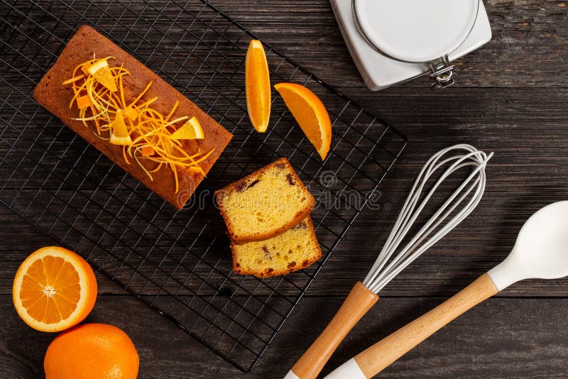 Orange pound cake on a cooling rack alongside a whisk, a spoon, a jar and oranges on dark vintage wood background, Flat lay royalty free stock images Orange pound cake on a cooling rack alongside a whisk, a spoon, a jar and oranges on dark vintage wood background, Flat lay royalty free stock images