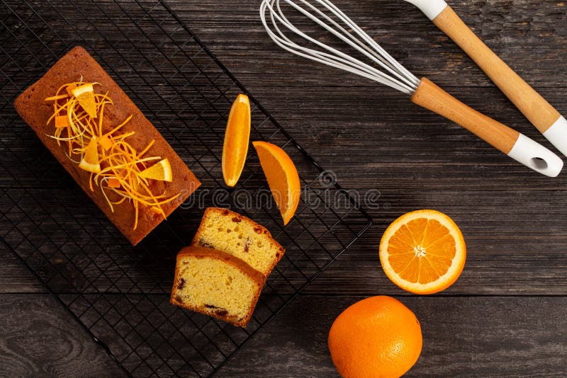 Orange pound cake on a cooling rack alongside a whisk, a spoon and oranges on dark vintage wood background, Flat lay stock photography Orange pound cake on a cooling rack alongside a whisk, a spoon and oranges on dark vintage wood background, Flat lay stock photography