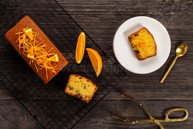 Orange pound cake on a cooling rack and slice on a plate alongside dessert tongs on dark vintage wood background, Flat lay royalty free stock photo Orange pound cake on a cooling rack and slice on a plate alongside dessert tongs on dark vintage wood background, Flat lay royalty free stock photo