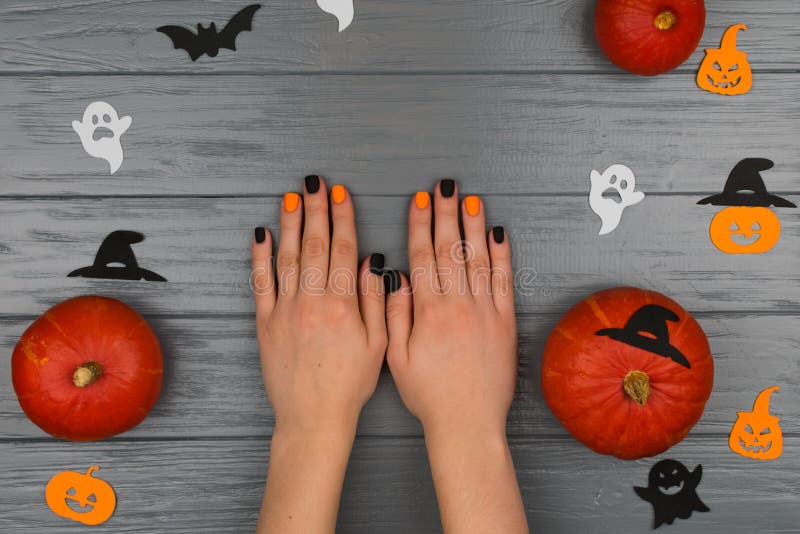 Orange pumpkins on a gray background. Female hands with autumn manicure on a gray background with orange pumpkins. Bats