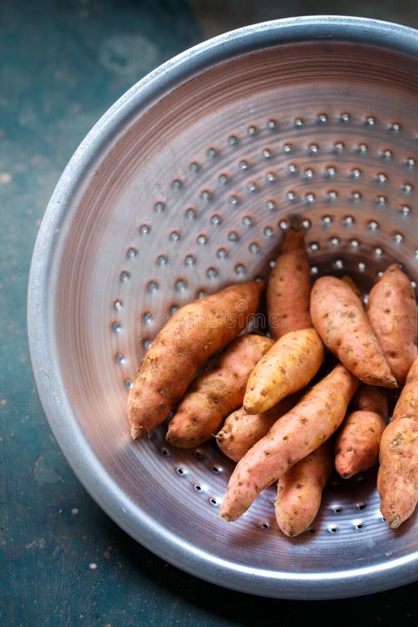 Orange sötpotatis i en metalldurkslag, närbild. Orange sötpotatis i en metalldurkslag på en mörk bakgrund