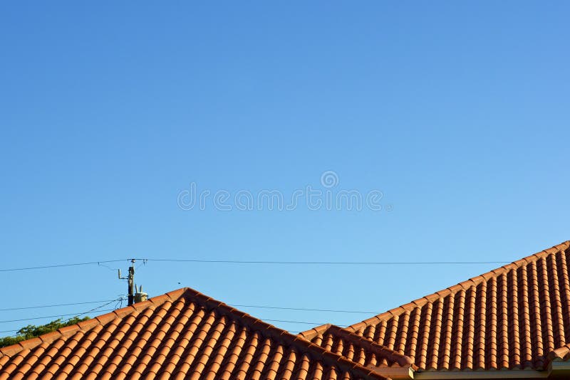 Orange terra cotta rooftop against blue sky with powerlines