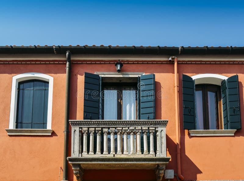 Orange wall of the house with a window with blue shutters and a balcony.