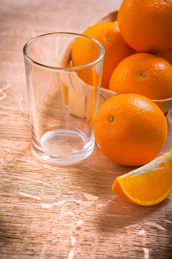 Oranges in bucket on wooden table with empty glass