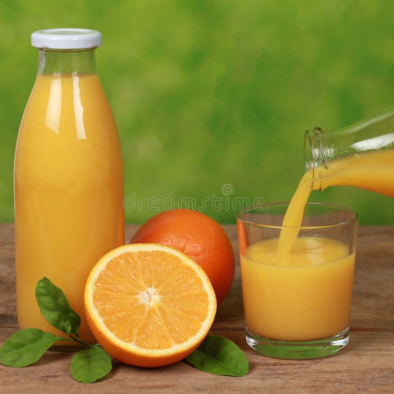 Oranges and fresh juice is pouring from a bottle into a glass on a wooden table