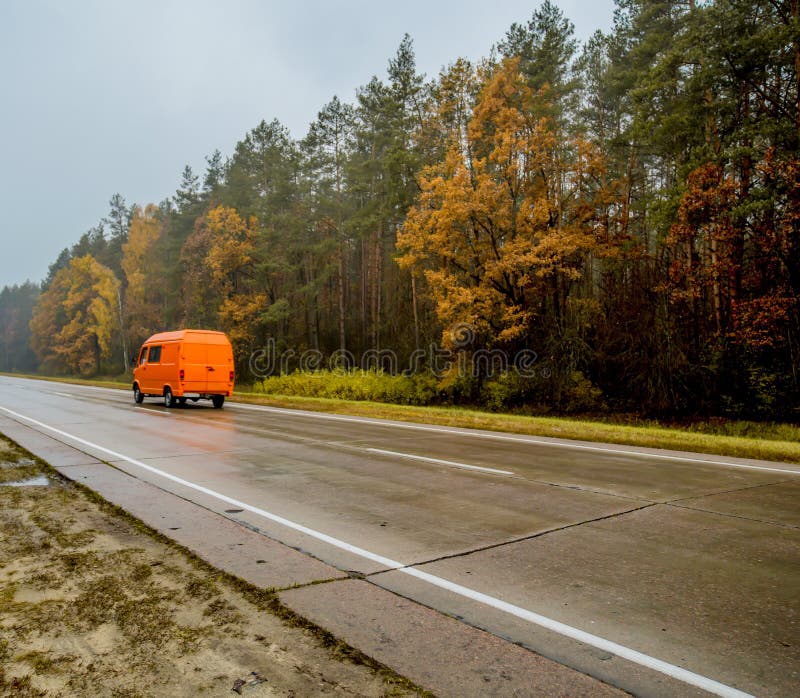 Oranje auto-bestelwagen, die langs de de herfstweg bij zonsondergang gaan stock foto Oranje auto-bestelwagen, die langs de de herfstweg bij zonsondergang gaan stock foto