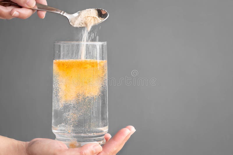 A person pouring orange powder into a glass of water with copyspace. A person pouring orange powder into a glass of water with copyspace