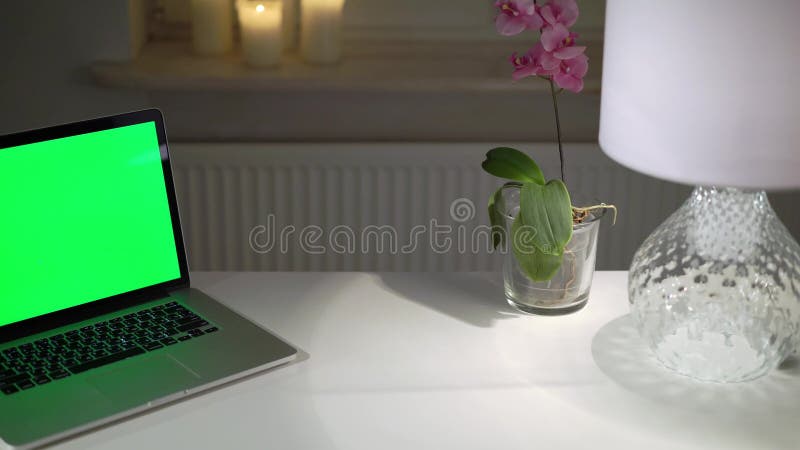 Ordenador portátil con pantalla verde en la mesa en la oficina del hogar por la noche