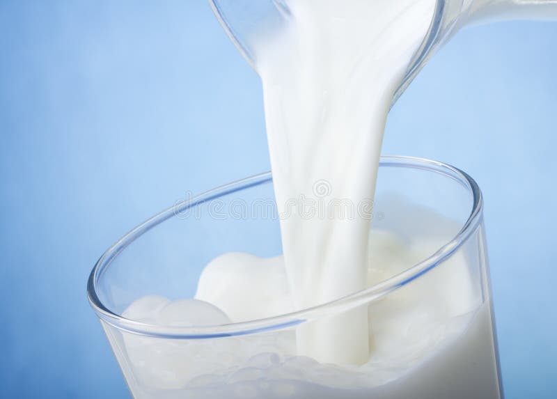 Milk pouring into glass on blue background. Milk pouring into glass on blue background