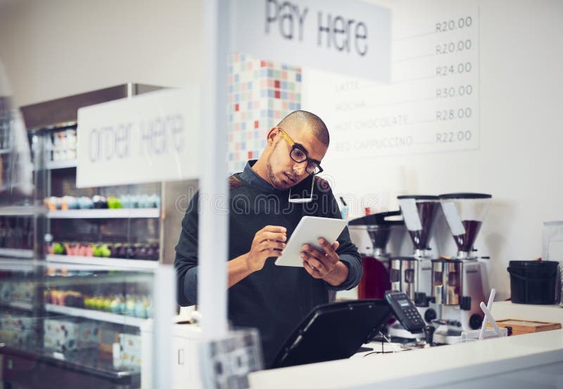 Ordering everything he needs to make great coffee. a man talking on his cellphone in a coffee shop while using a digital royalty free stock images