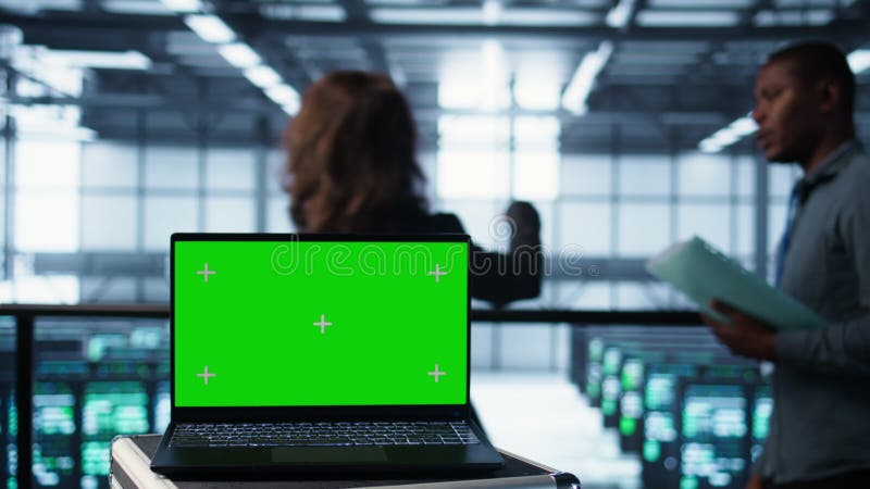 Ordinateur portable à écran vert devant les ingénieurs du datacenter inspectant les serveurs banque de vidéos