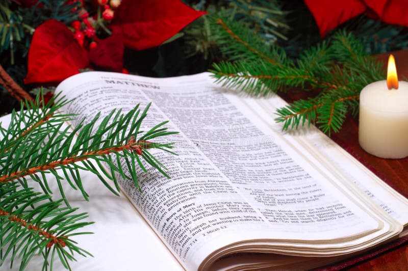 Bible open to the Christmas passage of Matthew 2 with candle, poinsettia, and evergreen sprigs. Bible open to the Christmas passage of Matthew 2 with candle, poinsettia, and evergreen sprigs