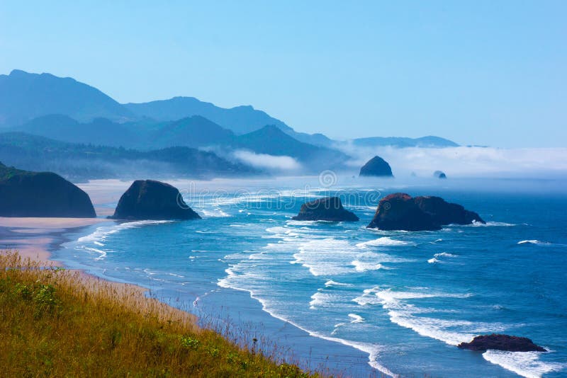 Bright clear blue sky on sunny day at Oregon coast Gentle waves against shoreline. Large coastal rocks and wild grasses in landscape view. Bright clear blue sky on sunny day at Oregon coast Gentle waves against shoreline. Large coastal rocks and wild grasses in landscape view.