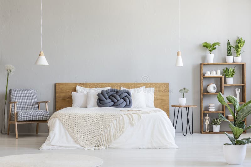 Blue knot pillow on wooden bed in modern bedroom interior with patterned armchair. Real photo. Blue knot pillow on wooden bed in modern bedroom interior with patterned armchair. Real photo