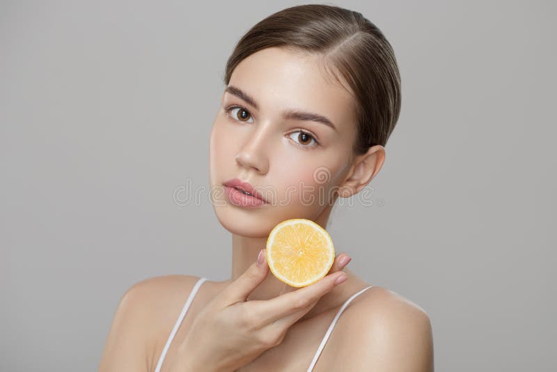 Organic cosmetics concept. A young girl with clean skin holds lemon slice near her face.