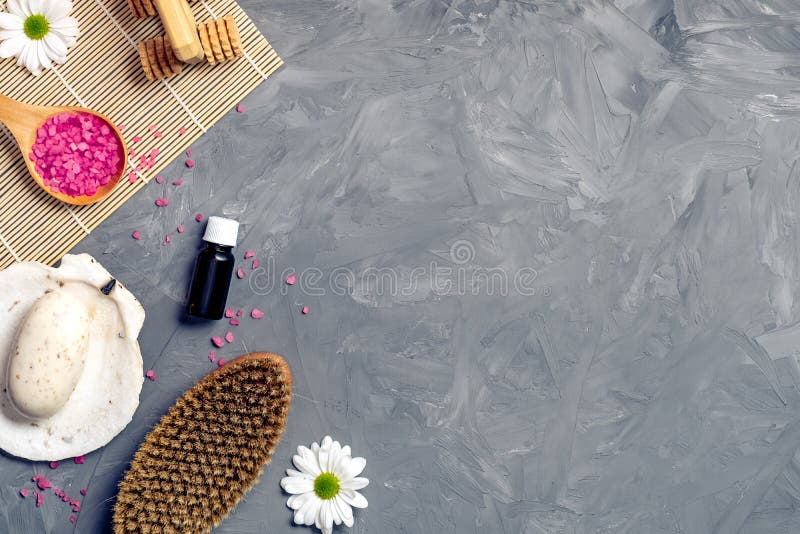 Organic spa cosmetic and products on grey stone background. Spoon with pink bath salt, body brush, organic soap, and flowers. Top